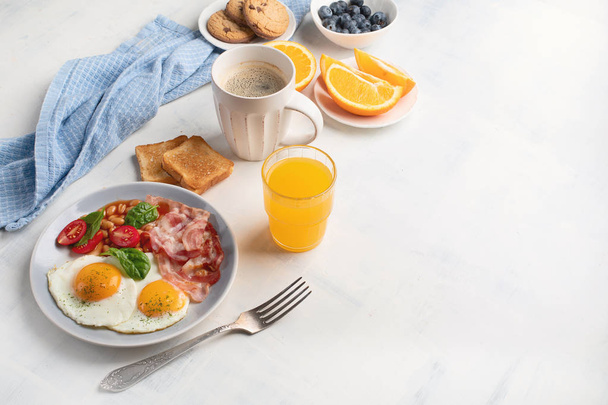 Breakfast with fried eggs, bacon, orange juice, yogurt and toasts. Top view with copy space - Foto, Bild