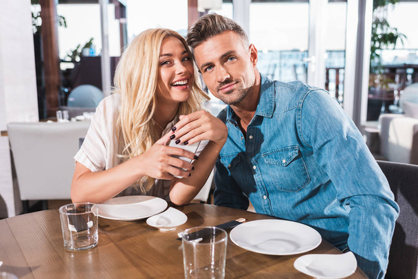 couple souriant étreignant et regardant la caméra à la table dans le café
  - Photo, image