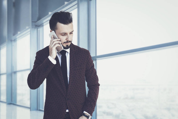 Trendy en modieuze zakenman in de corporate gebouw lopend en pratend aan de telefoon (gemengd) - Foto, afbeelding