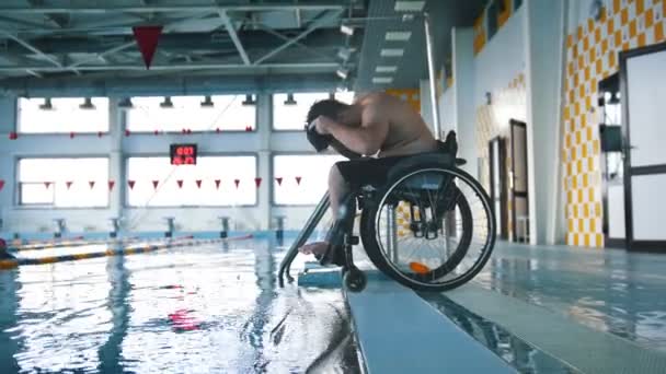 Vammainen mies pyörätuolissa laittamassa uimalakkia ja suojalaseja. Sivuttaiskulma
 - Materiaali, video