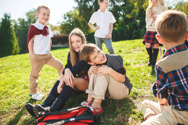 Μια ομάδα παιδιών σχολικής και προσχολικής ηλικίας κάθεται στο καταπράσινο γρασίδι στο πάρκο. - Φωτογραφία, εικόνα