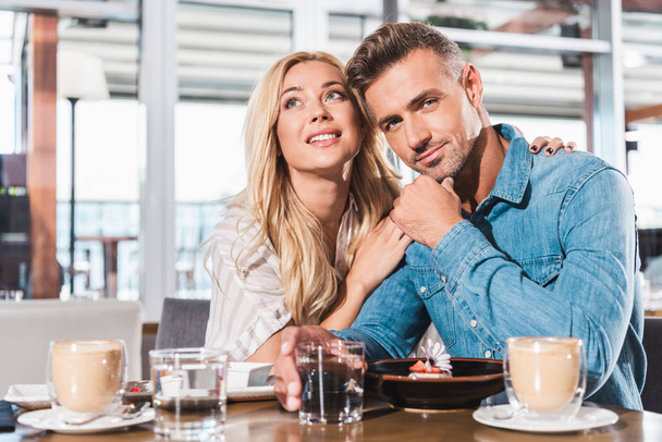 novia abrazando novio y él mirando la cámara en la mesa en la cafetería
 - Foto, Imagen