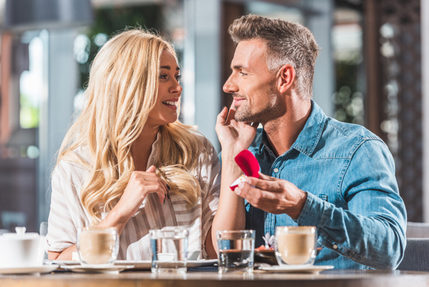 handsome boyfriend proposing surprised girlfriend and showing ring in cafe - Photo, Image