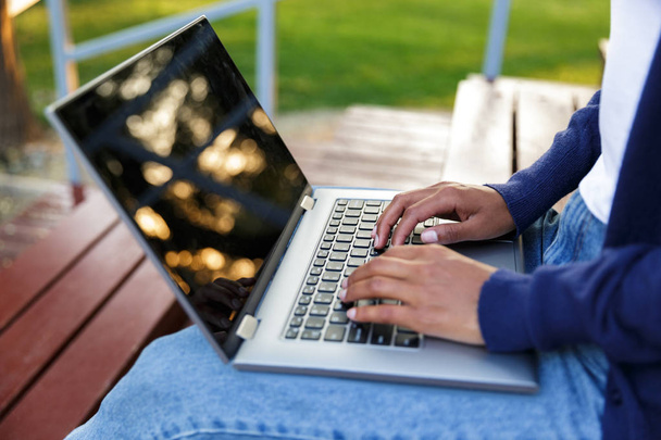 Cropped photo of african young woman sitting outdoors in park on steps using laptop computer. - Photo, Image
