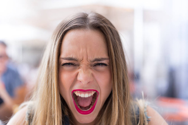 Wütende Frau schreit mit geöffnetem Mund und blickt in Kamera  - Foto, Bild
