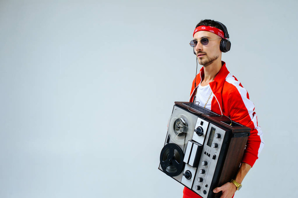 cheerful fashionable man wearing a red sports suit and headphones dancing jumps with a retro tape recorder. interesting and fervent style of the 90s. - Photo, Image