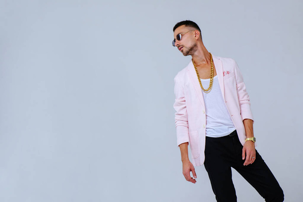 fashionable sophisticated man in a pink jacket and black trousers, wears a gold chain, the manifestation of emotions gestures hands space for text. - Foto, imagen