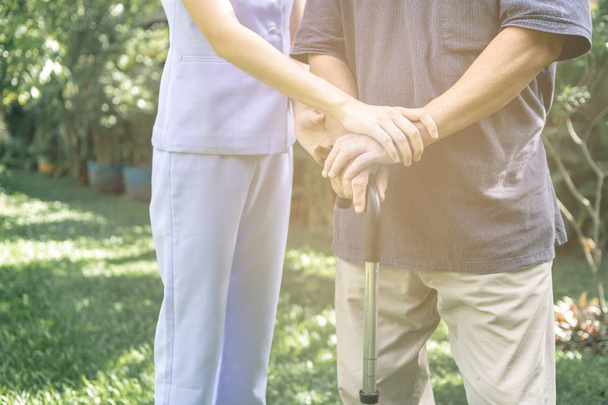 Comforting hand. Young nurse holding old man's hand in outdoor garden. Senior care, care taker and senior retirement home service concept. Close up shot. - Foto, Imagem