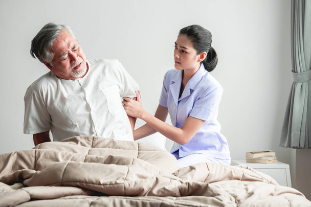 Senior man in bed trying to get up and nurse helping him. Old asian man and beautiful asian nurse woman in bedroom and open curtain. Senior home service concept. - Valokuva, kuva