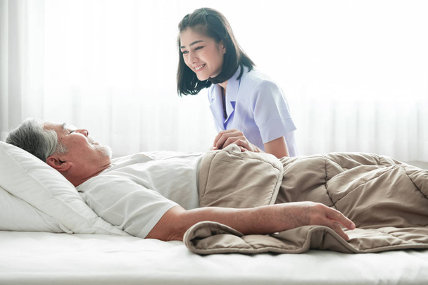 Senior man in bed and nurse woke him up. Old asian man and beautiful asian nurse woman in bedroom and open curtain. Senior home service concept. Close up shot. - Fotó, kép