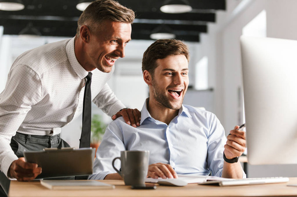 Image des hommes heureux émotionnels excités collègues au bureau travaillant avec l'ordinateur
. - Photo, image