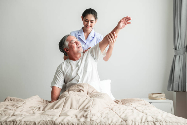 Young attractive physiotherapist working on senior man. Beautiful asian woman working with asian senior man's shoulder. Senior home caretaker service concept. - Foto, afbeelding