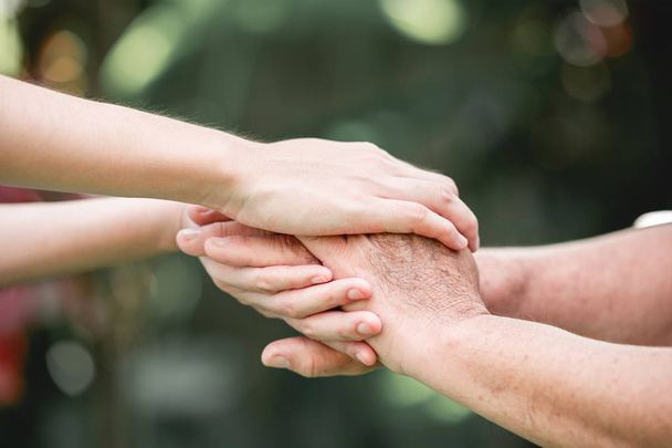 Comforting hand. Young nurse holding old man's hand in outdoor garden standing up. Senior care, care taker and senior retirement home service concept. - Foto, Bild