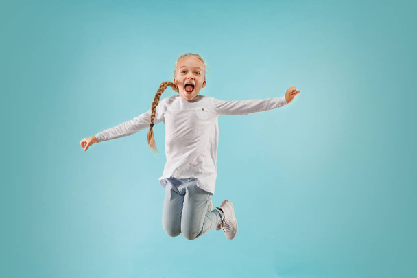 Adorable small child at blue studio. The girl is jumping and smiling. - Fotó, kép