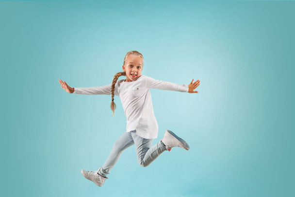 Adorable small child at blue studio. The girl is jumping and smiling. - Foto, Bild