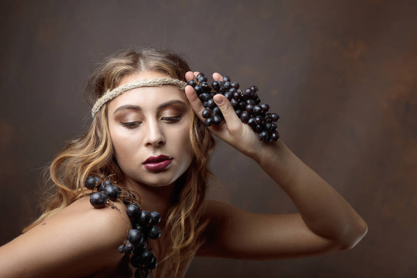 Portrait of blonde with blue grapes. Beautiful girl with long wavy hair and perfect make-up. - Foto, afbeelding
