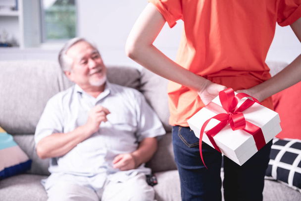 I got a present for you. Daughter giving her senior father a surprise present. Asian man with white beard and beautiful woman. Senior lifestyle concept. - Foto, Imagem