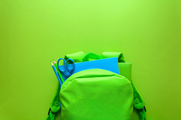 Back to school concept. Green backpack with school supplies on green background. Top view. Copy space - Valokuva, kuva