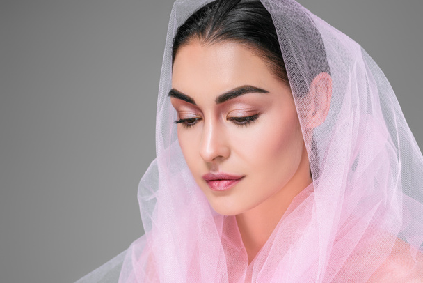 beautiful young woman with pink veil looking down isolated on grey - Foto, afbeelding