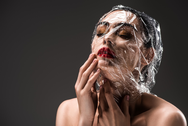 αισθησιακή γυναίκα με πρόσωπο τυλιγμένα σε διάφανο σελοφάν με σταγόνες που απομονώνονται σε μαύρο  - Φωτογραφία, εικόνα