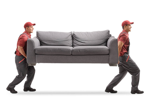 Full length profile shot of two movers carrying a couch isolated on white background - Фото, изображение
