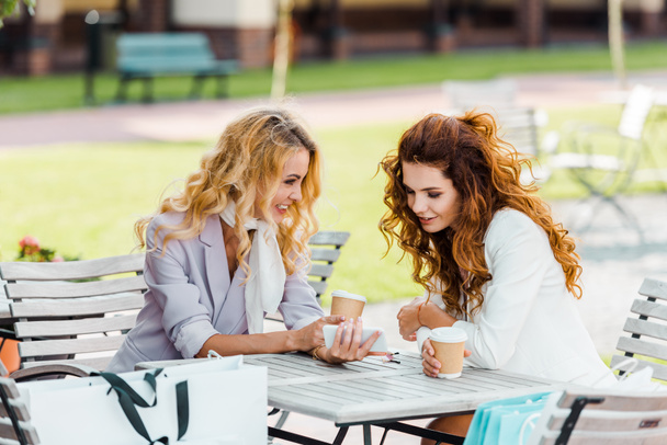 mujeres jóvenes atractivas utilizando el teléfono inteligente mientras pasan tiempo juntos en la cafetería después de ir de compras
 - Foto, imagen