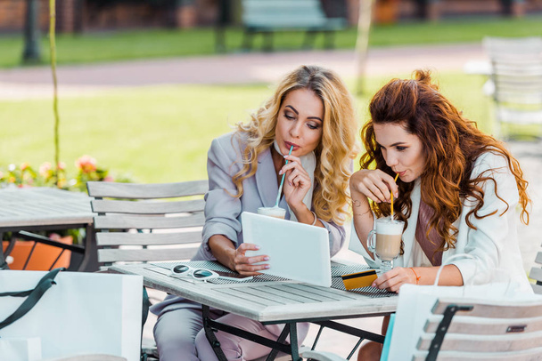 tyylikäs nuoret naiset luottokortilla ja tabletilla joten e-ostoksia istuu kahvilassa
 - Valokuva, kuva