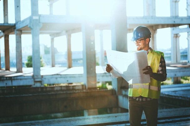 Portrait of male site contractor engineer with hard hat holding blue print paper at construction site, - Foto, afbeelding