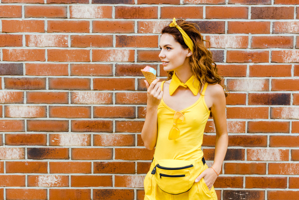 bella donna sorridente in abiti gialli con gelato in posa davanti al muro di mattoni
 - Foto, immagini