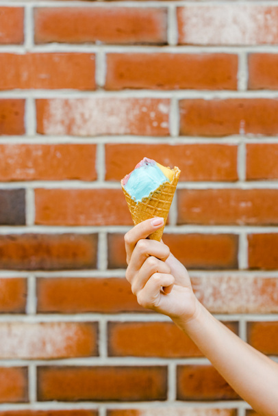 colpo ritagliato di donna che tiene il gelato nel cono cialda davanti al muro di mattoni
 - Foto, immagini