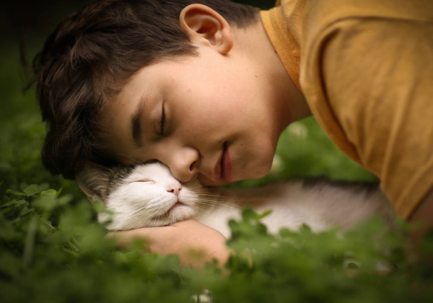 dospívající chlapec s cat polibek objetí na zelené letní trávy zblízka fotografie - Fotografie, Obrázek