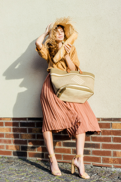 krásná mladá žena v slamák s bagetou stojící před bílou stěnu - Fotografie, Obrázek