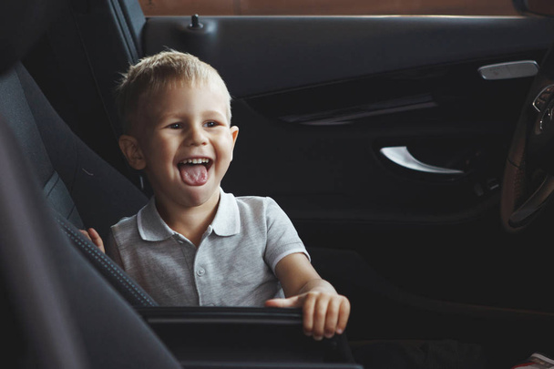Zabawny mały chłopiec siedzi w kabinie nowy samochód i jest szczęśliwy. Po prostu kupić samochód w centrum sprzedawcy. Pojęcie zakup pojazdu. - Zdjęcie, obraz
