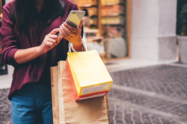Consumerism, shopping, lifestyle concept, Young woman holding colorful shopping bags and smartphone enjoying in shopping. - Photo, Image