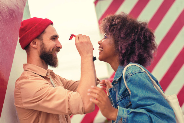 Bearded man smiling and holding red glasses of his cheerful girlfriend - Valokuva, kuva