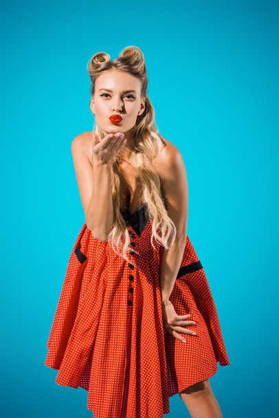 portrait of attractive pin up woman in retro style clothing blowing kiss on blue backdrop - Zdjęcie, obraz