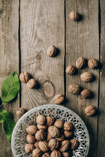 top view of ripe organic walnuts, green leaves and plate on wooden table - Foto, afbeelding