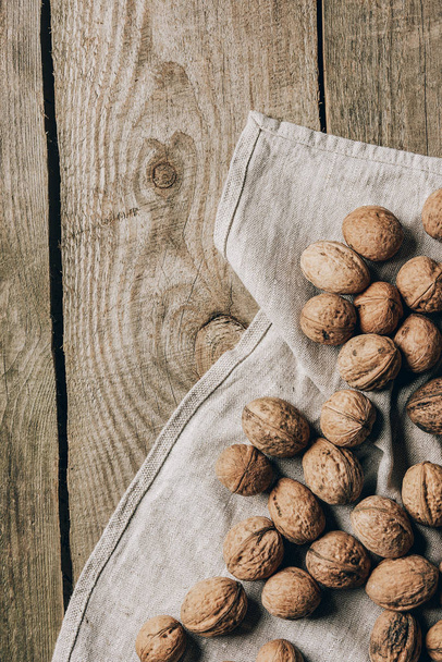 top view of whole tasty healthy walnuts on cloth on wooden table - Foto, Imagen