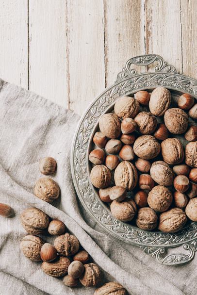 top view of hazelnuts and walnuts on vintage plate and sackcloth on wooden table - Photo, Image