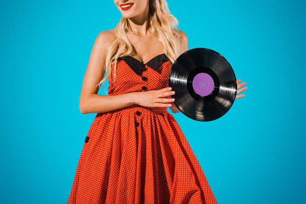 partial view of woman in vintage dress showing vinyl record on blue backdrop - Fotoğraf, Görsel