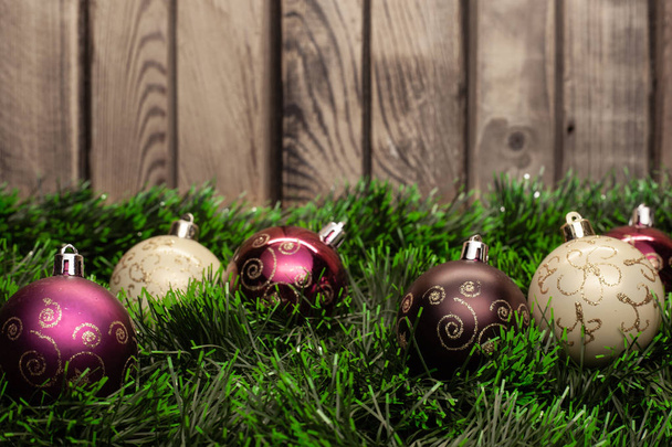 Christmas toy white ball and purple ball with patterns on green tinsel on a wooden background - Foto, Imagen