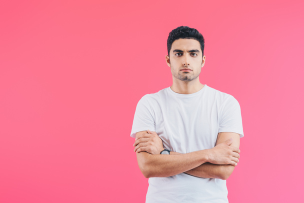 serious handsome man standing with crossed arms and looking at camera isolated on pink - 写真・画像
