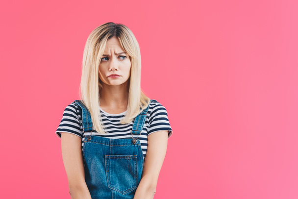worried beautiful girl in denim overall looking away isolated on pink - Photo, Image