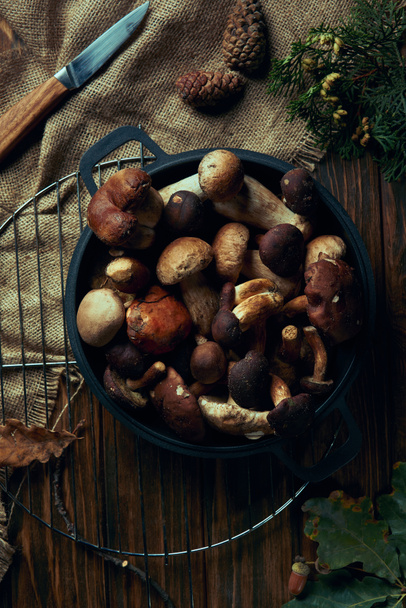 bovenaanzicht van geassorteerde rauwe champignons in de pan, mes en zak op houten tafel - Foto, afbeelding