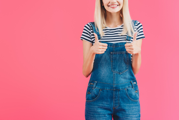 cropped image of smiling girl in denim overall showing thumbs up isolated on pink - Φωτογραφία, εικόνα