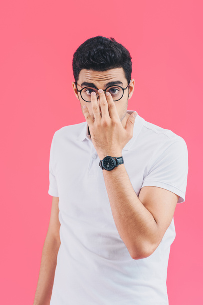 handsome man fixing glasses and looking at camera isolated on pink - Foto, afbeelding