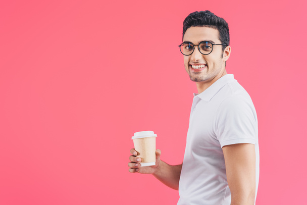 sonriente hombre guapo sosteniendo café para ir y mirando a la cámara aislado en rosa
 - Foto, imagen
