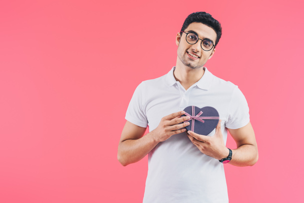 усміхнений красивий чоловік тримає подарункову коробку у формі серця поблизу серця ізольовано на рожевій концепції святого Валентина
 - Фото, зображення