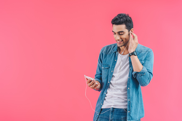 portrait of smiling man with smartphone listening music in earphones isolated on pink - Fotoğraf, Görsel