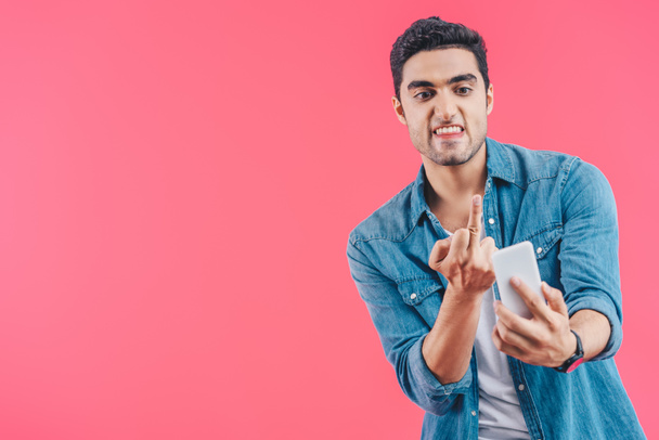 Portret van boze man toont middelvinger aan smartphone geïsoleerd op roze - Foto, afbeelding